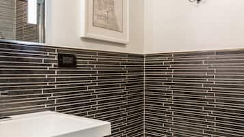 A modern bathroom with a white toilet, a sink with a wooden cabinet, and a black tiled backsplash.