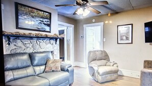 Un salon doté d’une cheminée en pierre, d’un ventilateur de plafond et d’un téléviseur fixé au mur.