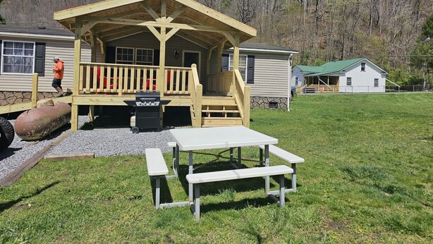 Une cabane en bois avec une véranda, un barbecue et des tables de pique-nique.