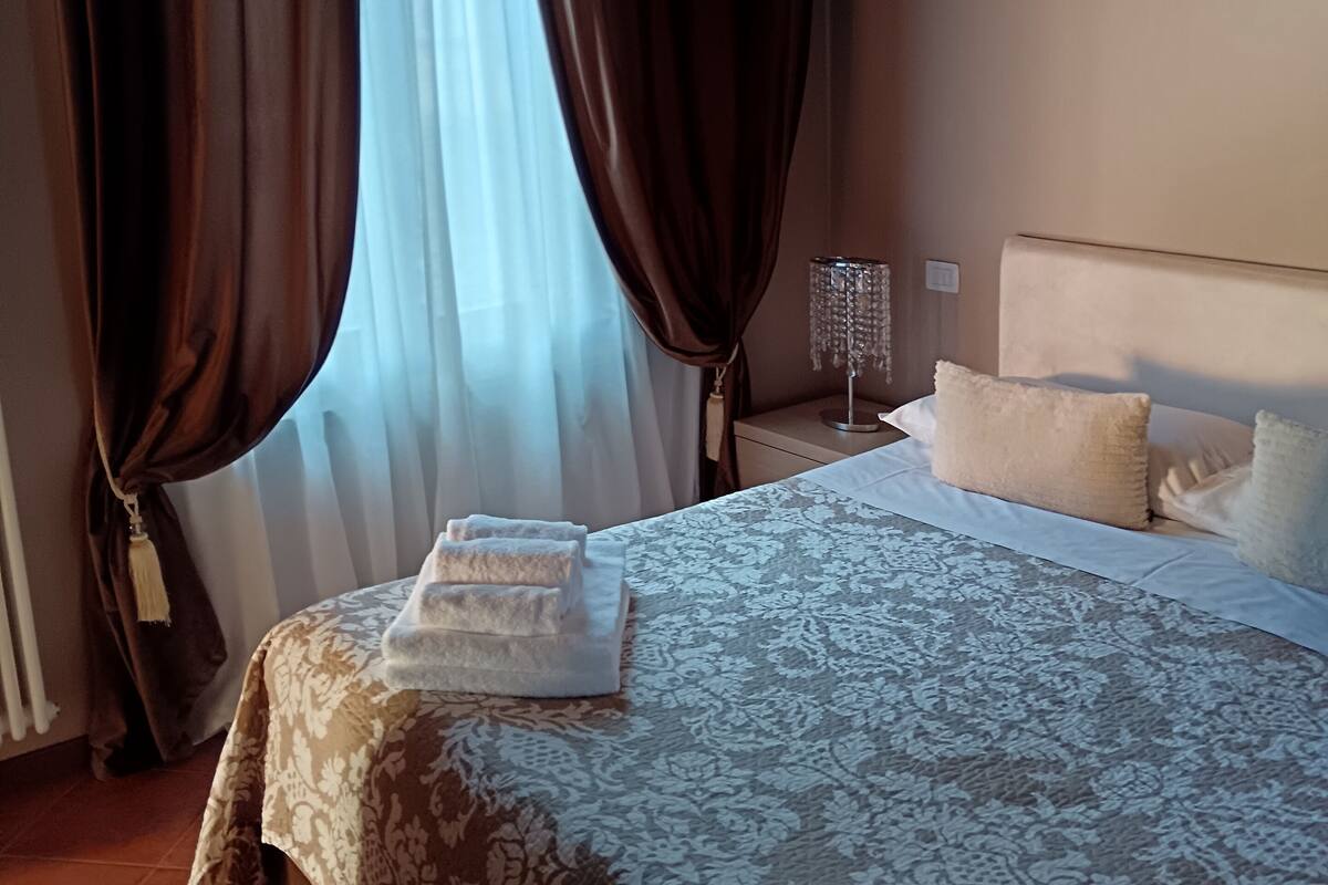 A bedroom with a bed, curtains, a nightstand, and a bedside lamp.
