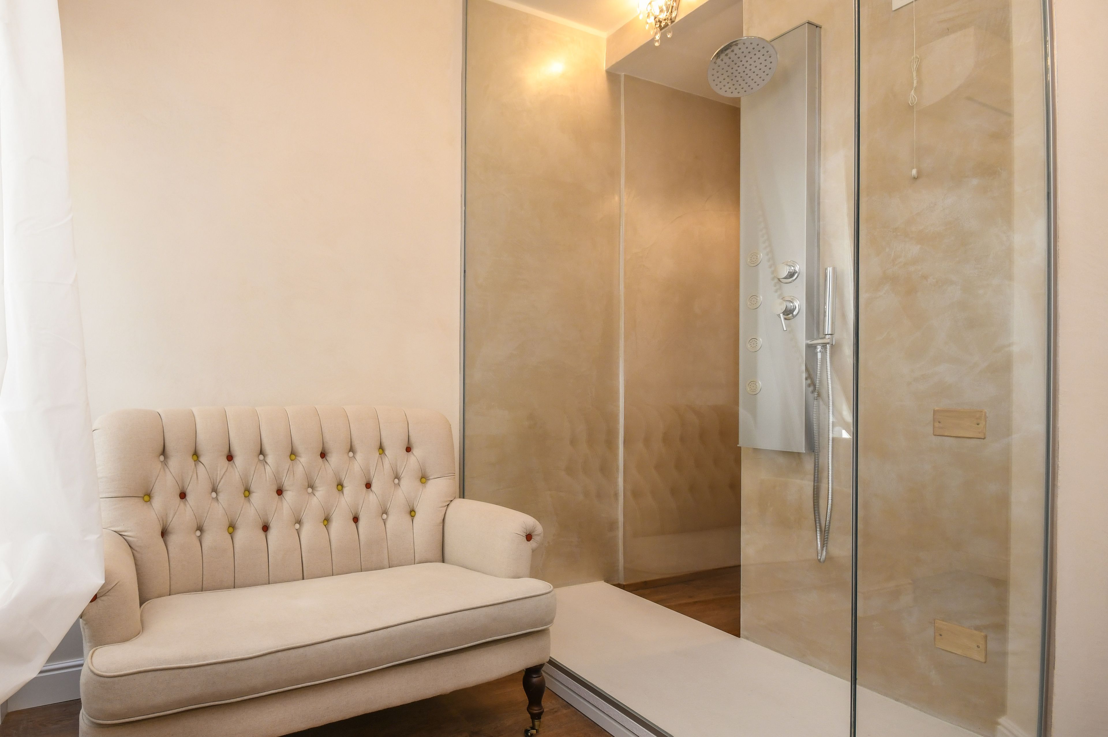 A modern bathroom with a glass-enclosed shower, a beige sofa, and a wooden floor.