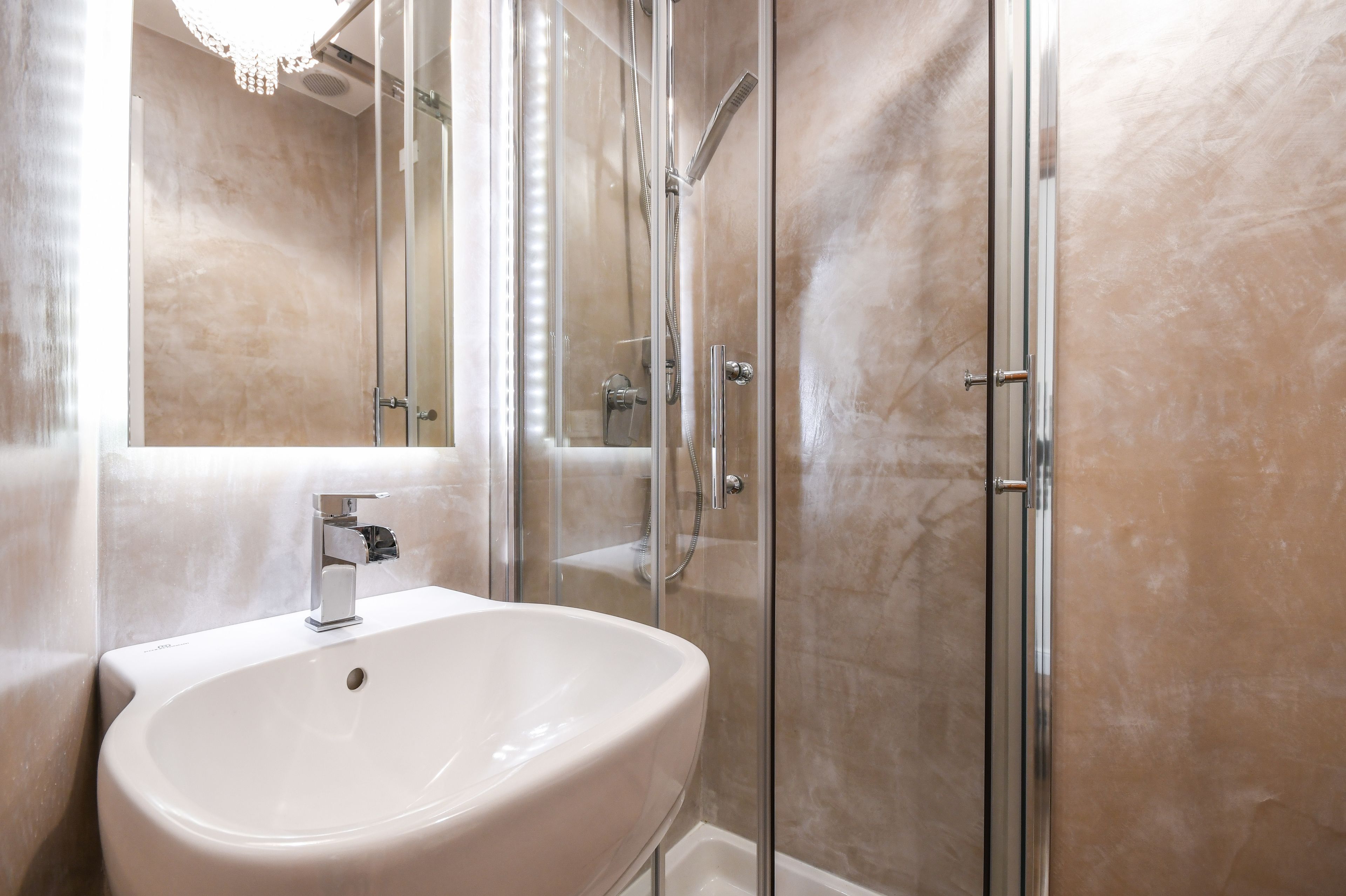 A bathroom with a white sink, a glass shower enclosure, and a marble wall.