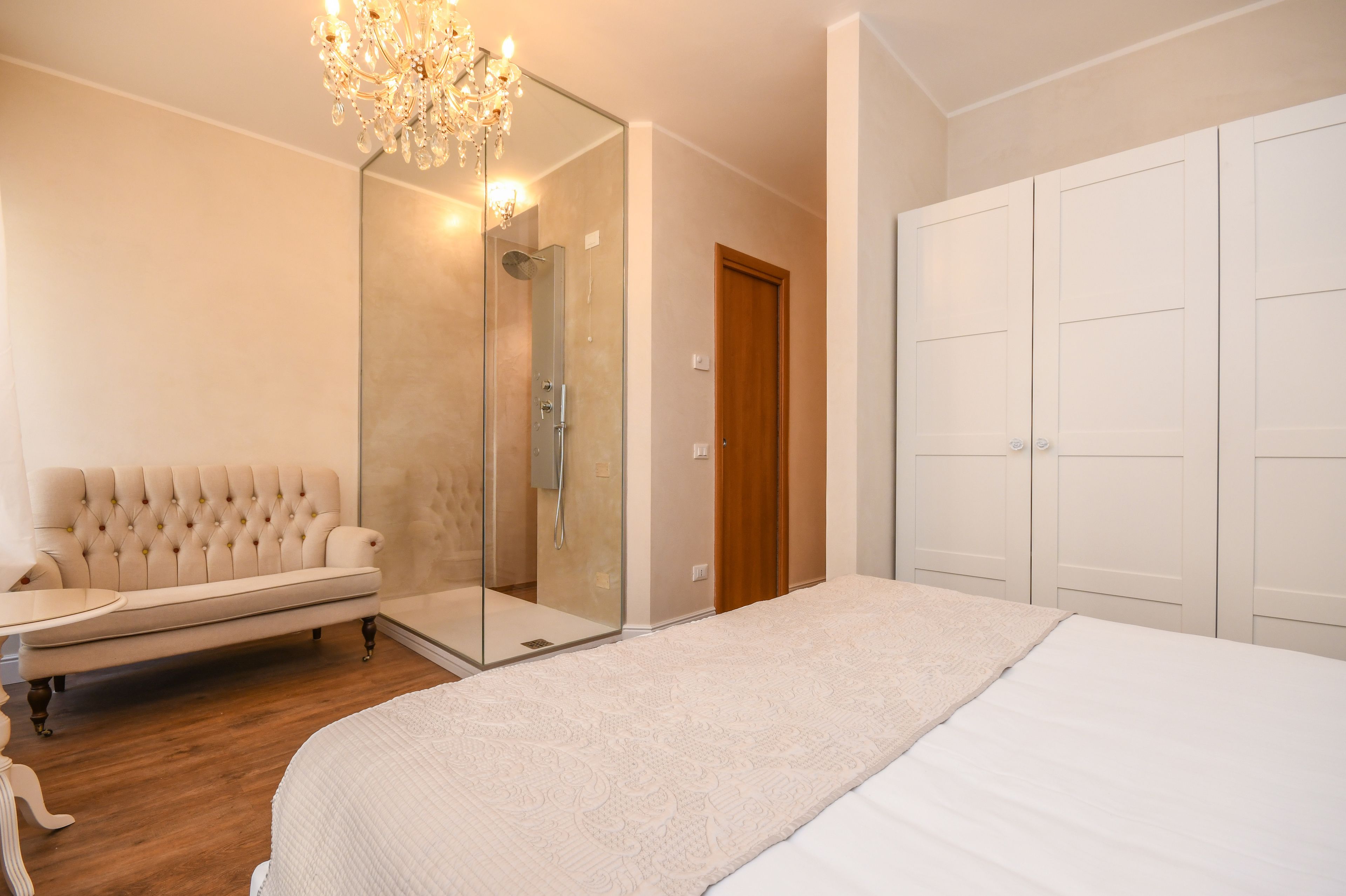 A bedroom with a large bed, a glass shower enclosure, a tufted sofa, and a wardrobe.