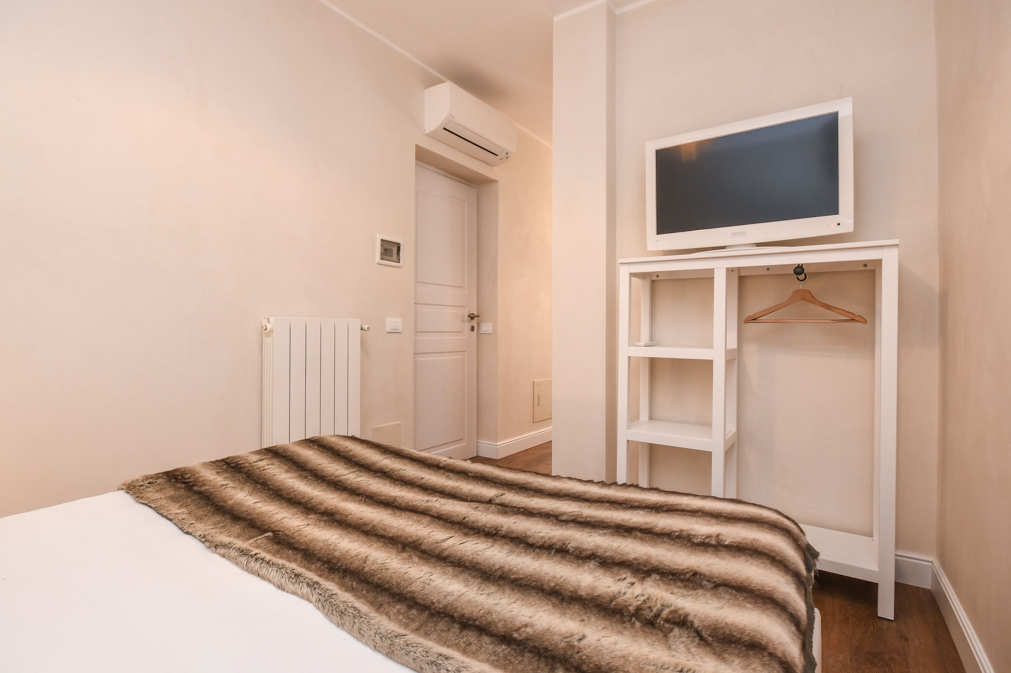Ein Schlafzimmer mit einem Bett, einem Fernseher auf einem Schrank, einem Heizkörper und einer Tür.