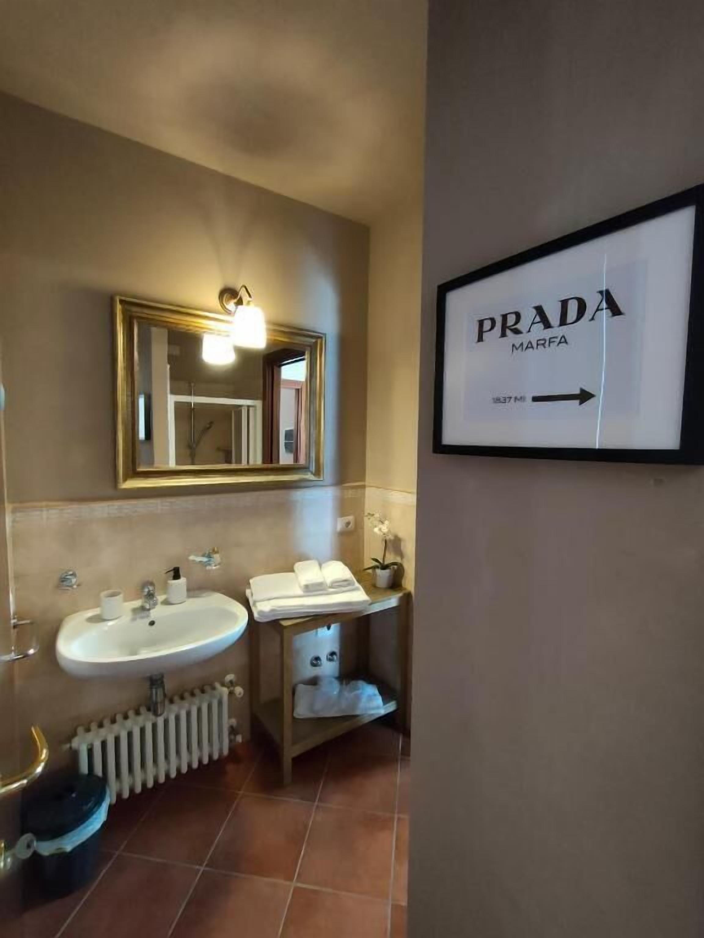 A bathroom with a large mirror, two sinks, a radiator, and a sign for Prada Marfa.