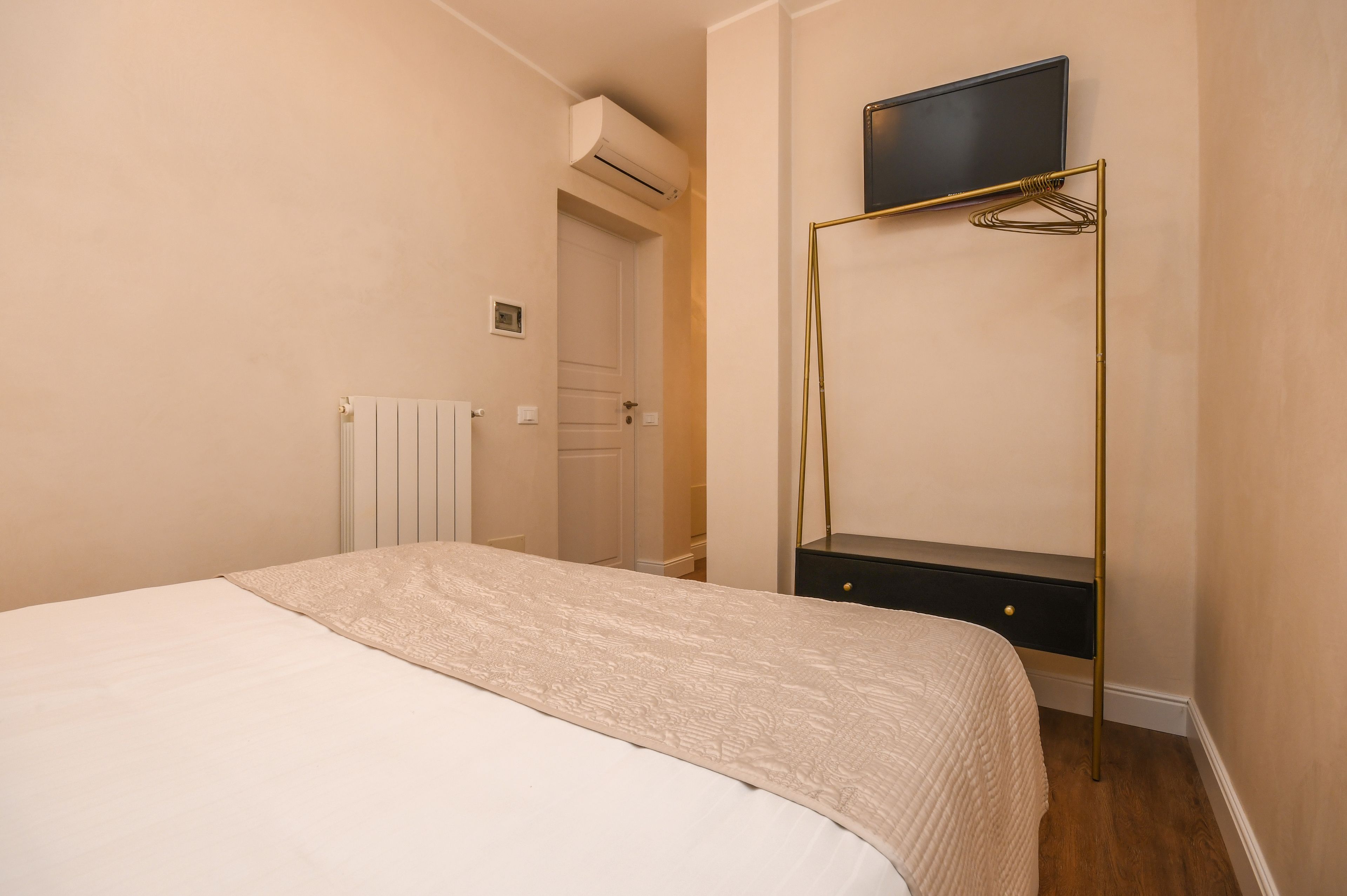 Une chambre à coucher comprenant un lit, une table de chevet, un téléviseur fixé sur un support doré et un appareil de climatisation.