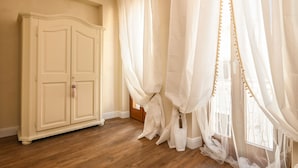 Una habitación con suelo de madera, un armario color crema y cortinas blancas traslúcidas.