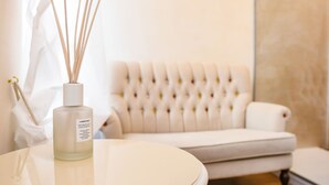 Una mesa blanca con un difusor de aroma de caña y una silla blanca en una habitación con respaldo capitonado.