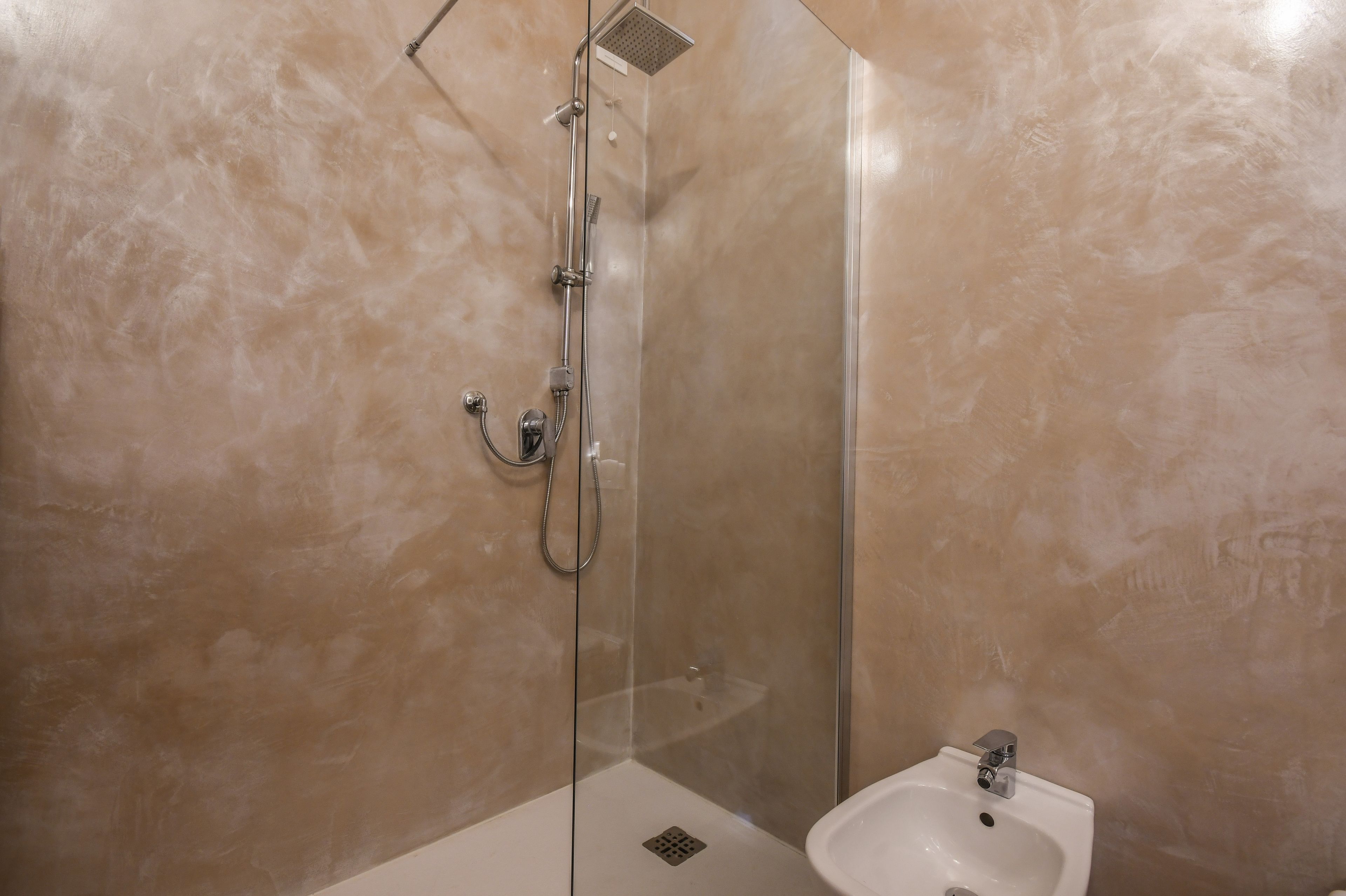 Ducha envuelta en vidrio con cabezal de ducha manual y grifo empotrado.
