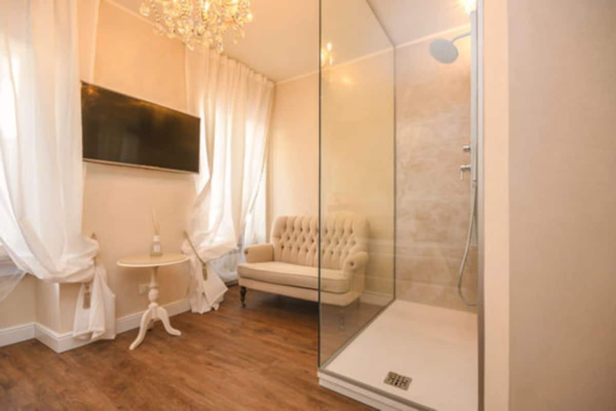 A modern bathroom with a glass shower enclosure, a white sofa, and a small table with a bottle.