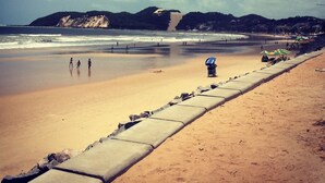 Une plage avec une promenade en béton, des gens qui se promènent et quelques parasols.