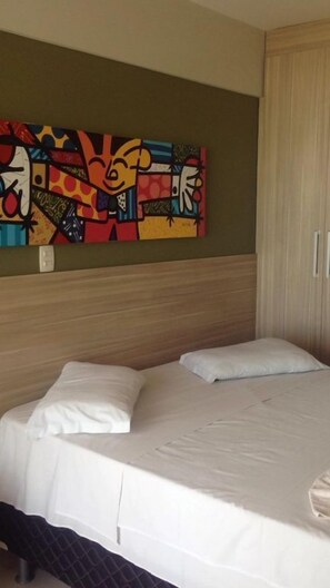 Une chambre d’hôtel avec un lit, un tableau abstrait aux couleurs vives accroché au mur et une armoire en bois.