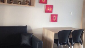 Un salon moderne avec un canapé foncé, une table basse en bois et trois chaises noires. Trois tableaux rouges sont accrochés au mur.