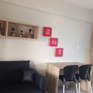 A modern living room with a dark sofa, a wooden coffee table, and three black chairs. There are three red paintings on the wall.