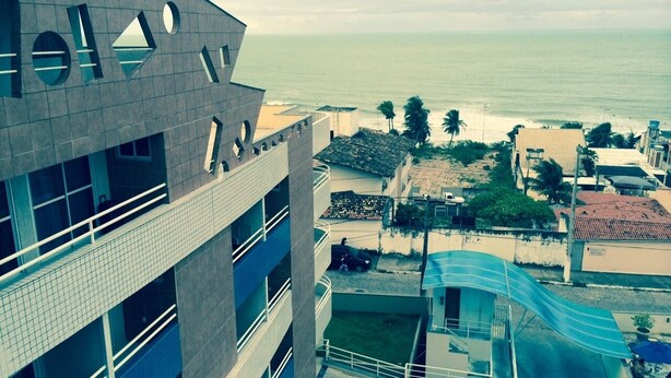 Un immeuble de grande hauteur doté d’une architecture moderne, comprenant un espace piscine avec toboggan et offrant une vue sur la plage et l’océan.