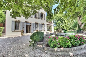 A two-story building with a gravel driveway and a circular flower bed with pink flowers. - Bastide for rent 10 min from Aix-en-Provence amidst vineyards (Aix-en-Provence)