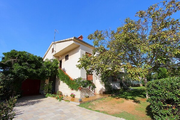 A two-story house with a red door, a stone staircase, and a garden with various plants and a small pond.