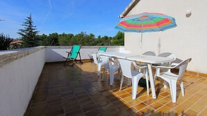 Una terrazza sul tetto con tavolo e sedie, un ombrellone colorato e una sedia pieghevole verde.
