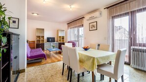 Una camera d'hotel con zona pranzo, TV, divano e balcone con tende.