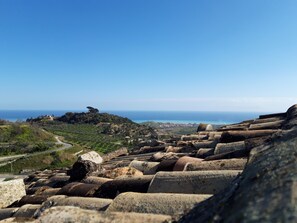 Un paysage côtier avec des constructions en pierre, une route sinueuse et une vue lointaine sur la mer.