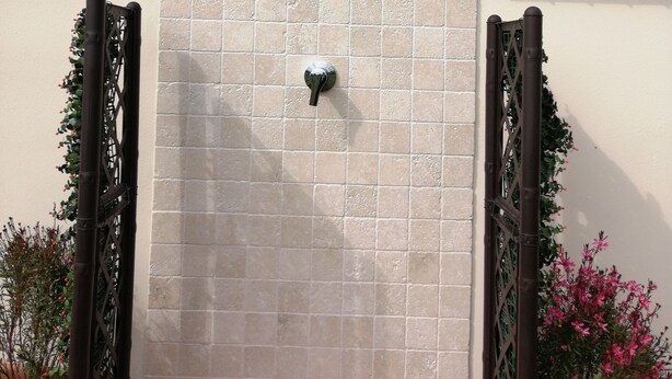 Une façade d’immeuble avec un mur recouvert de carreaux, un portail en métal et une fenêtre ornée d’une grille métallique.