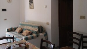 Un coin repas avec une table dressée pour deux personnes, un canapé et une porte donnant sur une autre pièce.