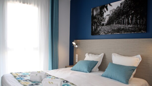 A hotel room with a bed, a nightstand, a lamp, and a painting on the wall. - Appartement Neuf et équipé, près des Antilles (Jonzac)