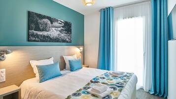 Wake up in the double bed, framed by blue curtains and a piece of artwork on the wall