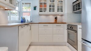 Moderni keittiö, jossa on valkoiset kaapit, sisäänrakennettu uuni ja ikkuna, josta avautuu näkymä vehreään maisemaan.