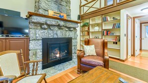 A cozy living room with a stone fireplace, a television, a bookshelf, and a comfortable seating area.