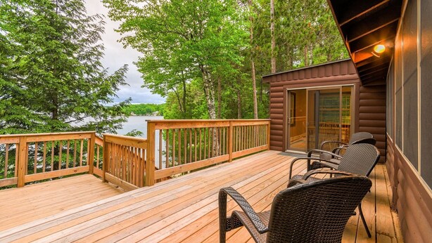 A wooden deck with a view of a lake, surrounded by trees.