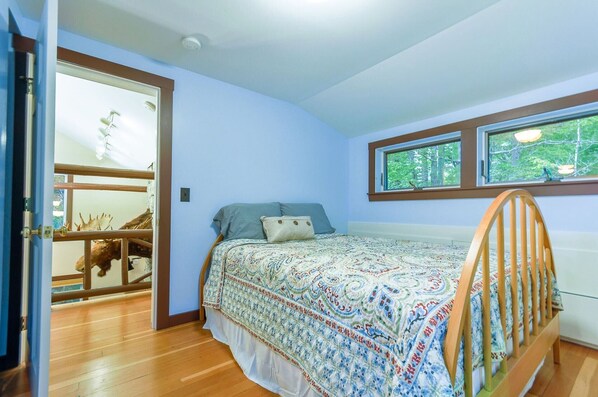 Un dormitorio con cama, ventana y puerta que da a una habitación con suelo de madera y estante con objetos decorativos.