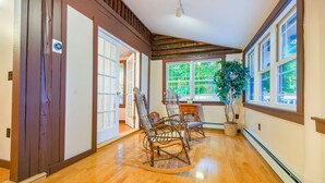 A spacious hallway with wooden flooring, a wooden-framed ceiling, and large windows offering a view of greenery outside.