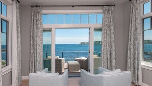A room with a large sliding glass door leading to a balcony with wicker furniture and a view of the sea.