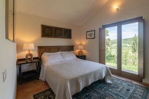 Un dormitorio con una cama grande, dos mesitas de noche con lámparas, un tapete estampado y vistas a zonas verdes a través de una puerta corredera.