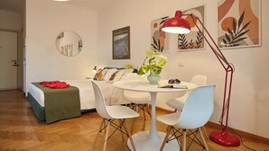 A modern room with a bed, a round mirror, a dining table with chairs, a red floor lamp, and abstract wall art. - Colourful apartment  St. Peter's View (ROMA)