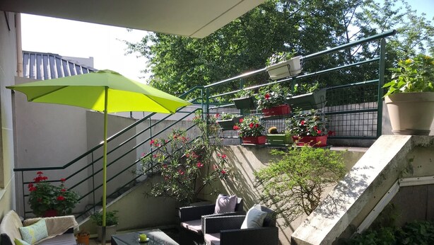 A balcony with outdoor furniture, a green umbrella, and potted plants.