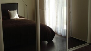 A bedroom with a bed, a hanging light fixture, a window with sheer curtains, and a view of the outdoors.