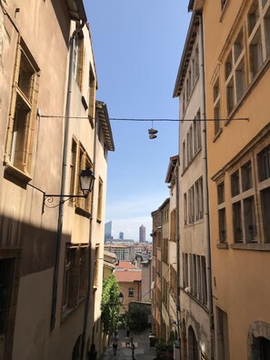 Rua estreita em área urbana, com edifícios em ambos os lados, céu claro e um par de sapatos pendurados em um fio.