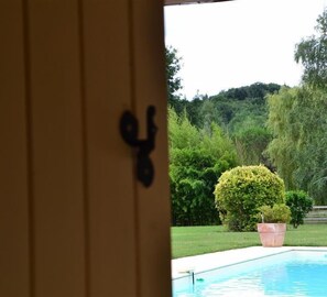 Vistatge a través d'una porta amb nansa negra, que dona a una zona de piscina amb un arbust ben podat i una banya gran.