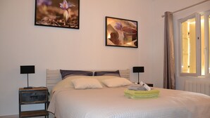 Una cama bien hecha con edredón blanco, dos mesitas de noche con lámparas y obras de arte en las paredes.