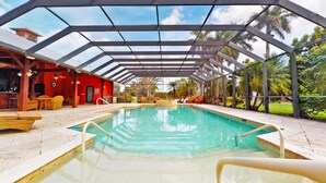 A covered swimming pool with a red building and outdoor seating area in the background. - Casa Tranquila Miami, A Luxury Ranch-Style Retreat (Miami)