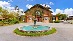 A large house with a fountain in front, surrounded by lush greenery and a clear blue sky. - Casa Tranquila Miami, A Luxury Ranch-Style Retreat (Miami)