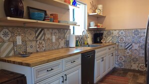 Cocina con armarios blancos, lavavajillas, encimera de madera y azulejos de refuerzo con diseño.