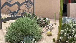 Un jardín desértico con diversos cactus y una escultura metálica frente a una pared con textura.
