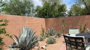 Un patio con pared de ladrillo, varios cactus y una mesa con sillas.