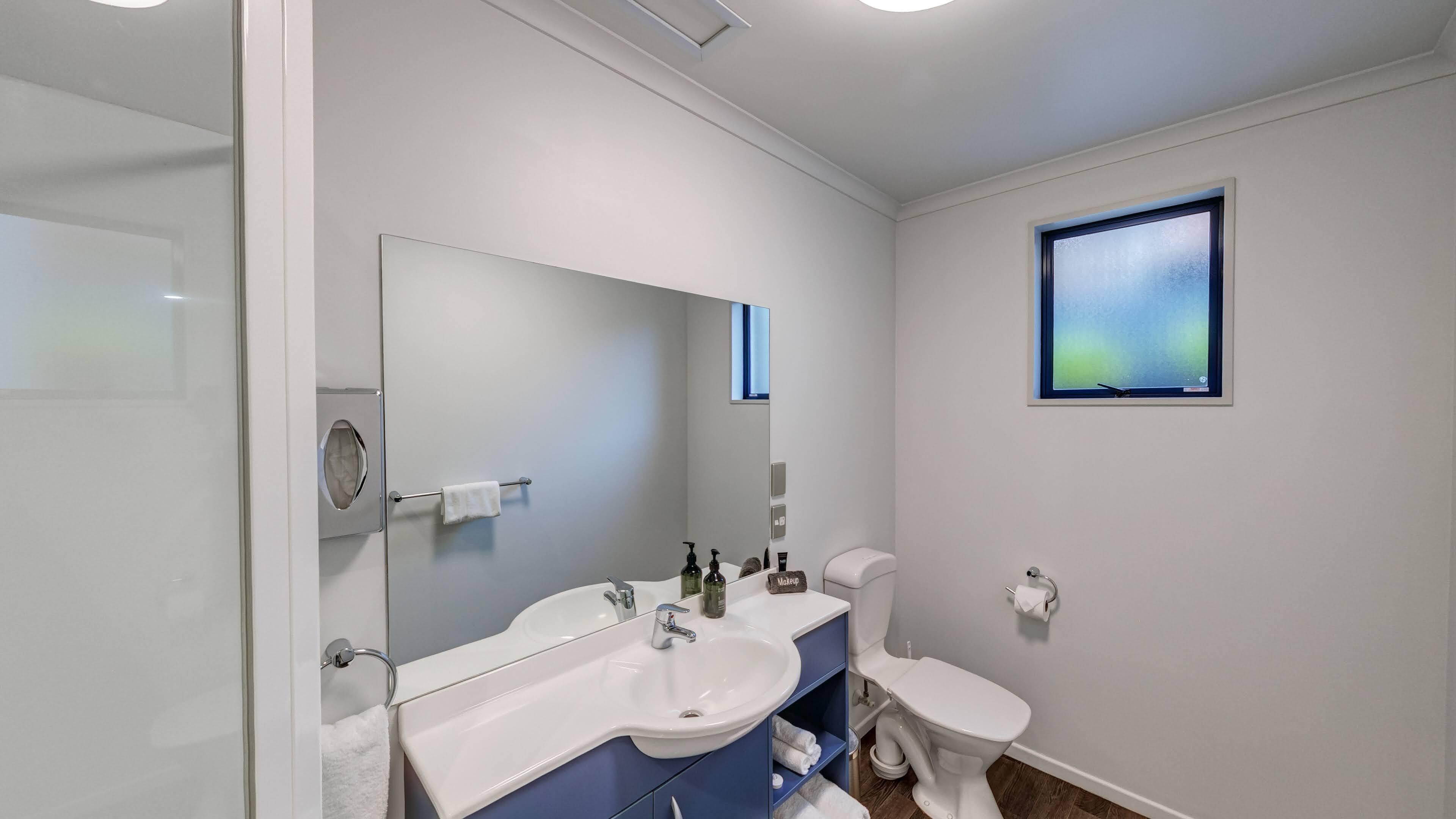 A modern bathroom with a white sink, a large mirror, a toilet, and a small window.