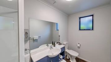 A modern bathroom with a white sink, a large mirror, a toilet, and a small window.