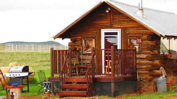 A rustic log cabin with a porch, a grill, and a small table with chairs. - Colorado Cabin with Hot tub, sauna, cold plunge! (Colorado)