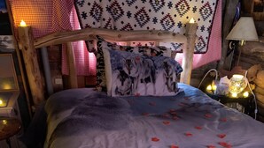 A wooden bed with a blue blanket and rose petals, surrounded by a rustic decor with a patterned wall and a lamp. - Colorado Cabin with Hot tub, sauna, cold plunge! (Colorado)